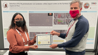 Anuva Anannya and Alexander Stewart hold a best poster award together at the Geological Society's annual conference. Anuva's award-winning poster on Mars is in the background. 