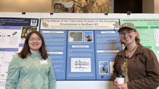 two female students smiling while presenting their poster