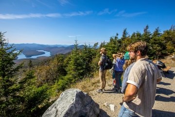 A group of students stand at a ledge overlooking Adirondack mountains and lakes.