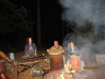 Len Mackey leads a drum circle around the fire, flanked by Arcadians Finn and Auti.
