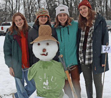  Julia Hahne ’26, Audrey Bowman ’24, Bryn Rodgers ’26, and Liz Anderson ’26 standing with their snowman fromthe Potsdam Town contest. Snowman is wearing a "SLU Sustainability Farm" T-Shirt