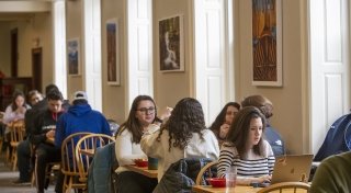 Students sitting down together for a meal and a discussion at several tables throughout Dana Dining Hall.