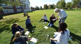 A professor works with a group of students while teaching an art class outdoors.