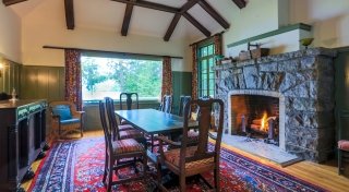 An Adirondack style meeting room with a large grey stone fire place with a roaring fire. A large picture window looks out on a bright sunny day.
