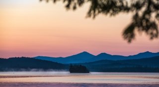Upper Saranac Lake as the sunsets over blue mountains.