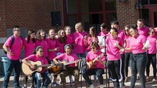 A group of Saint Lawrence students, wearing pink t-shirts, perform a musical number with instruments and a microphone, at the First-Year Cup Alma Mater Remix Competition. 