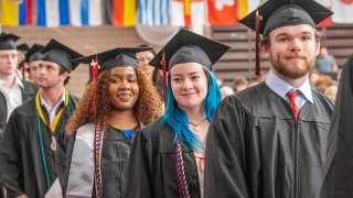 Photo of multiple students smiling as they stand in the processional line at commencment 2024.