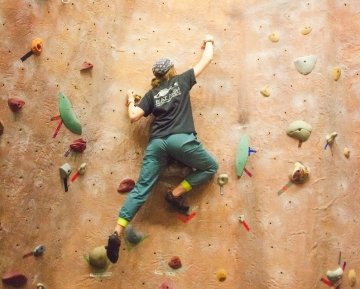 A student carefully makes their way up a climbing wall. 