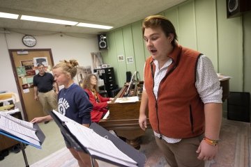 Two students sing into overhead microphones while reading music.