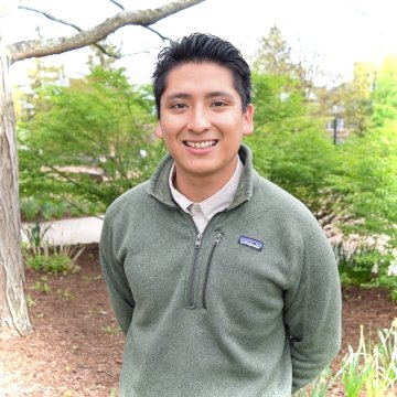 Headshot of Robertson Ramos Flores, standing against a background of trees and wearing a green patagonia quarter-zip sweatshirt.