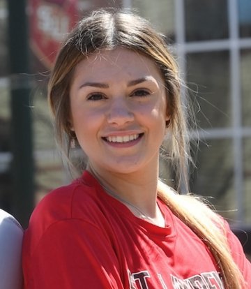 Headshot of Abby Doin, with her hair pulled back, wearing a red t-shirt that say "St. Lawrence" in large block letters.