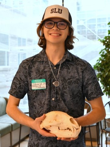 Edward Habeck, wearing a brown and white SLU hat, with a patterned button-down t-shirt, holding an animal skull.