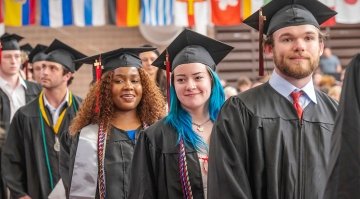 Photo of multiple students smiling as they stand in the processional line at commencment 2024.