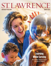 The cover of Saint Lawrence University Magazine reads, learning while serving. A Saint Lawrence student works alongside young students as they look at a large silver orb.